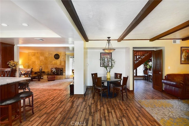 dining area featuring beam ceiling, dark wood-type flooring, and a tiled fireplace