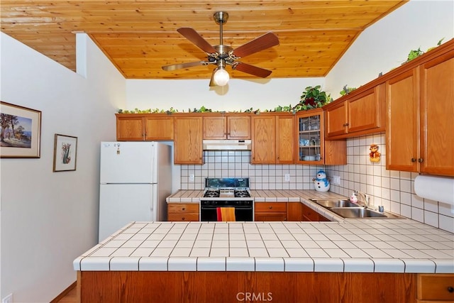 kitchen with sink, tile counters, white fridge, kitchen peninsula, and gas stove