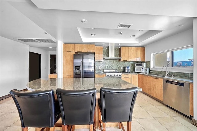 kitchen featuring wall chimney exhaust hood, stainless steel appliances, a raised ceiling, sink, and a kitchen island