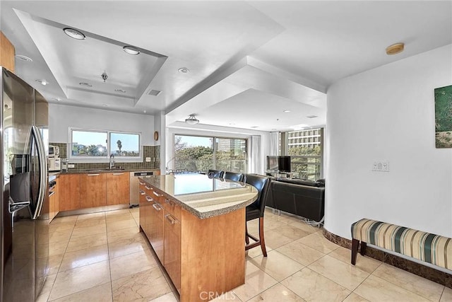 kitchen featuring decorative backsplash, appliances with stainless steel finishes, a breakfast bar, a raised ceiling, and a kitchen island