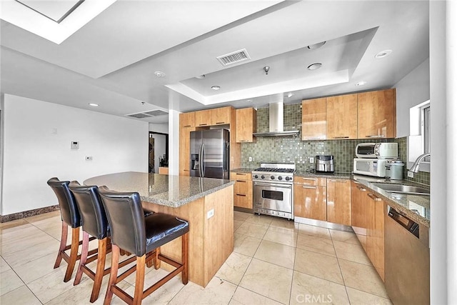 kitchen with sink, wall chimney exhaust hood, a kitchen island, a kitchen bar, and stainless steel appliances