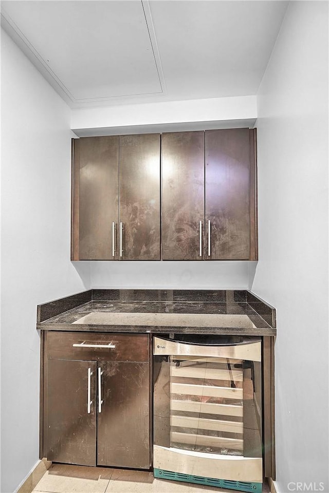 bar with dark brown cabinetry, wine cooler, and dark stone countertops