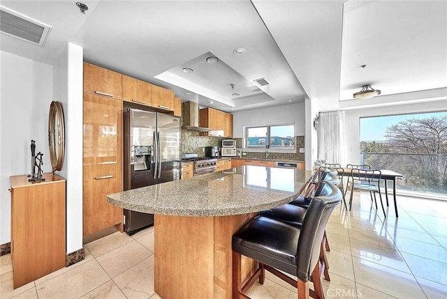 kitchen featuring a kitchen bar, stainless steel appliances, a wealth of natural light, and wall chimney exhaust hood