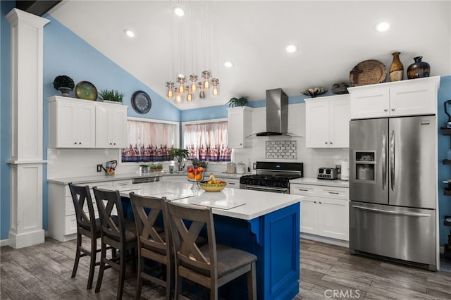 kitchen featuring wall chimney range hood, stainless steel appliances, a kitchen island, and vaulted ceiling