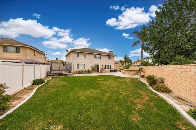 rear view of property with a trampoline, a patio area, and a lawn