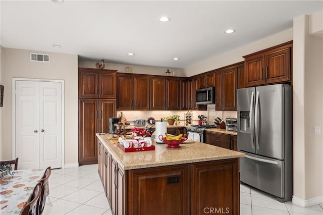 kitchen with a center island, stainless steel appliances, tasteful backsplash, light stone counters, and light tile patterned floors