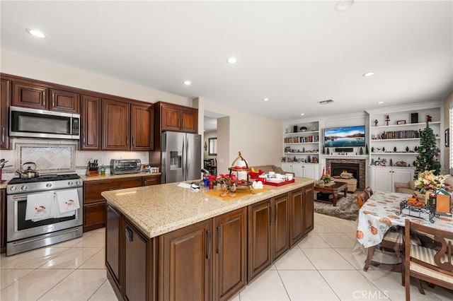 kitchen featuring a center island, backsplash, light stone countertops, light tile patterned floors, and appliances with stainless steel finishes