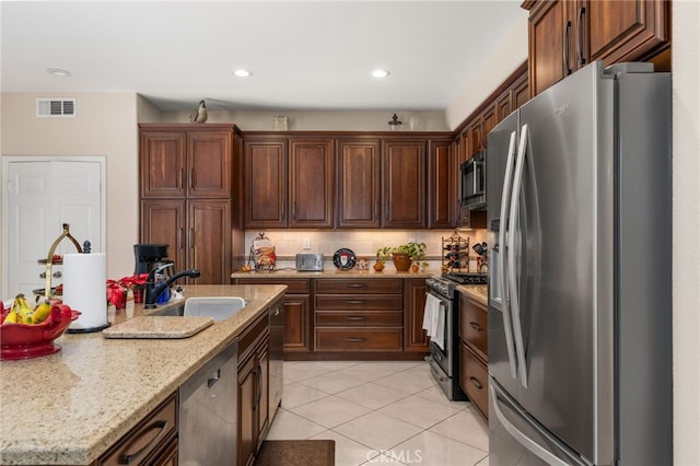 kitchen with decorative backsplash, light stone counters, stainless steel appliances, sink, and light tile patterned floors