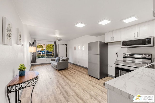 kitchen with light stone countertops, light wood-type flooring, stainless steel appliances, ceiling fan, and white cabinets