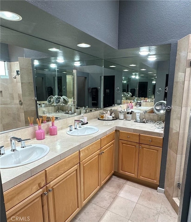 full bathroom with tiled shower, double vanity, and a sink