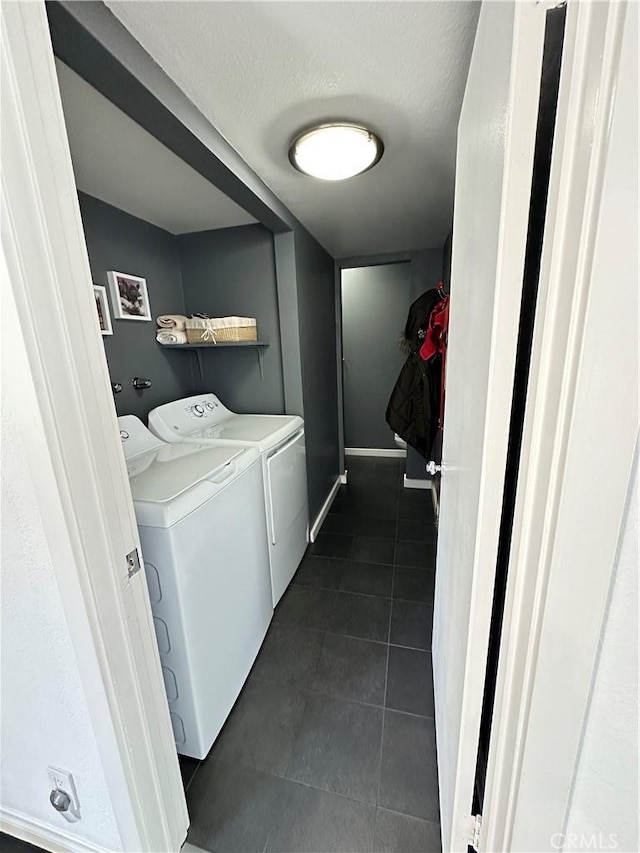 clothes washing area featuring washing machine and dryer, laundry area, baseboards, and dark tile patterned flooring