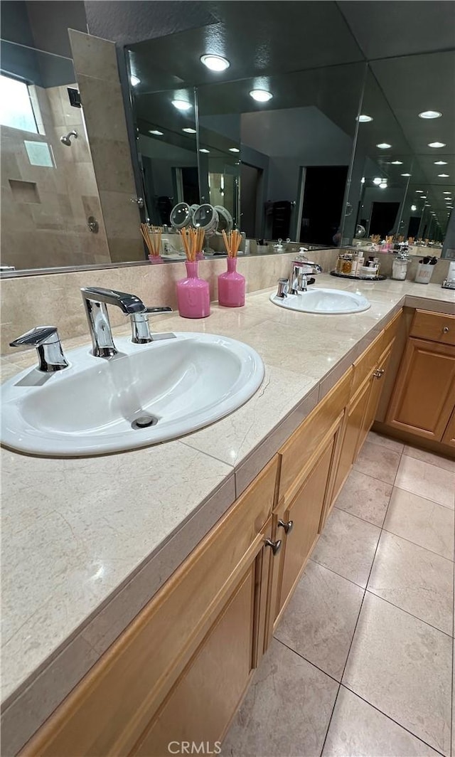 full bath with tile patterned flooring, double vanity, a tile shower, and a sink
