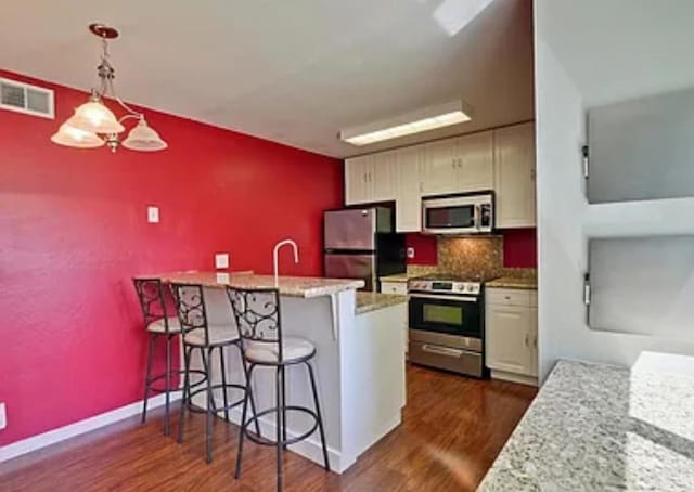 kitchen with appliances with stainless steel finishes, decorative light fixtures, backsplash, a kitchen bar, and dark wood-type flooring