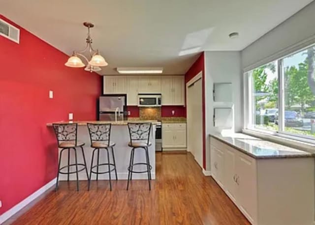 kitchen with pendant lighting, an inviting chandelier, stainless steel appliances, a kitchen breakfast bar, and wood-type flooring