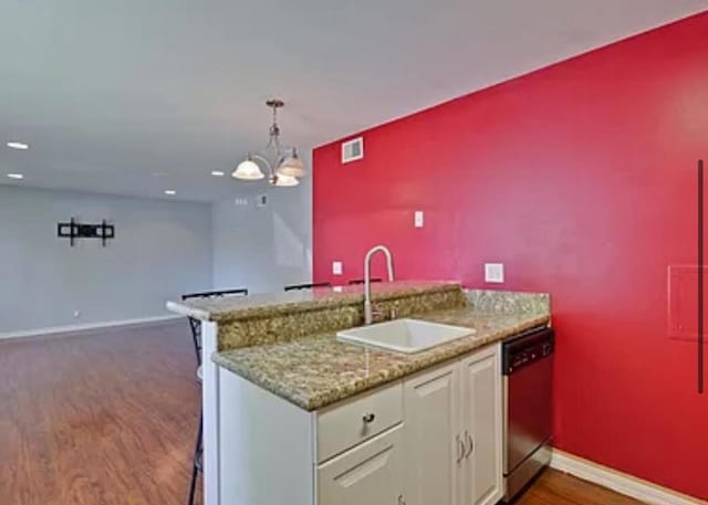 kitchen with sink, hanging light fixtures, stainless steel dishwasher, dark hardwood / wood-style floors, and light stone countertops