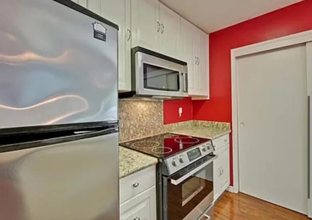 kitchen featuring tasteful backsplash, light stone counters, stainless steel appliances, light hardwood / wood-style floors, and white cabinets