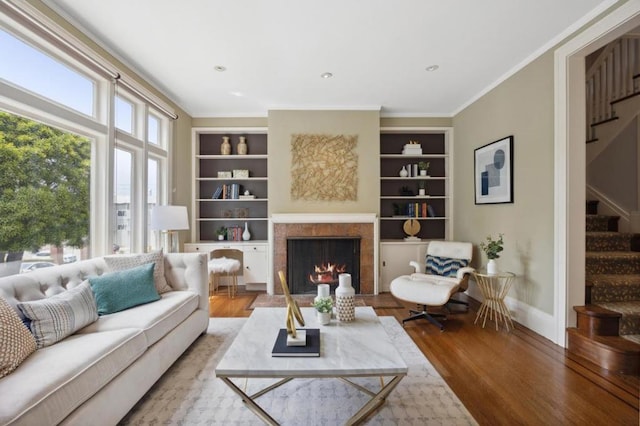 living room with built in shelves, a tiled fireplace, and hardwood / wood-style floors