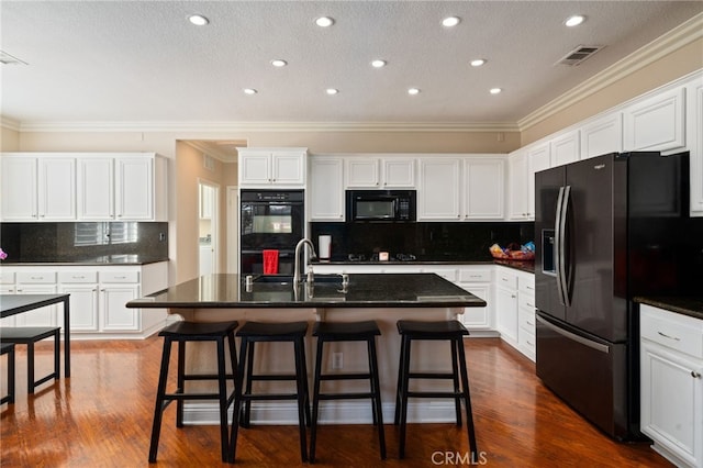 kitchen featuring black appliances, dark hardwood / wood-style floors, a center island with sink, and tasteful backsplash