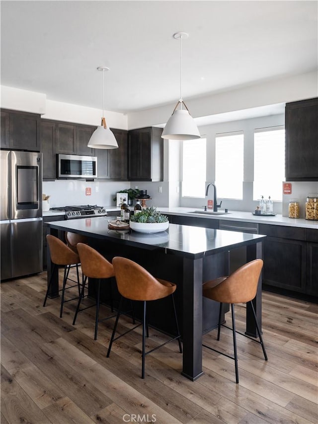 kitchen featuring appliances with stainless steel finishes, light wood-type flooring, decorative light fixtures, and a center island