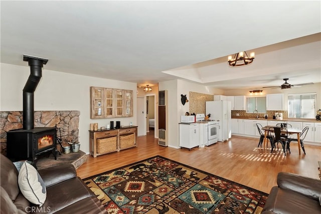 living room with ceiling fan with notable chandelier, light hardwood / wood-style floors, a wood stove, and sink