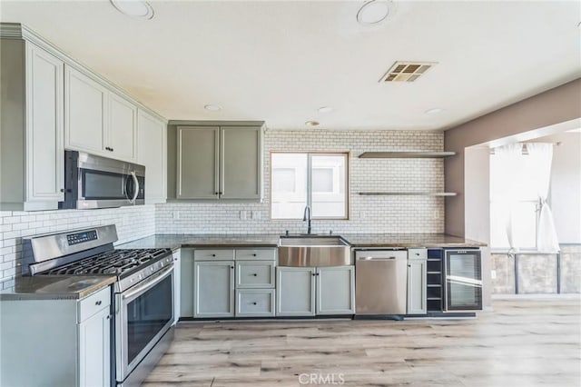 kitchen with sink, beverage cooler, tasteful backsplash, appliances with stainless steel finishes, and light wood-type flooring