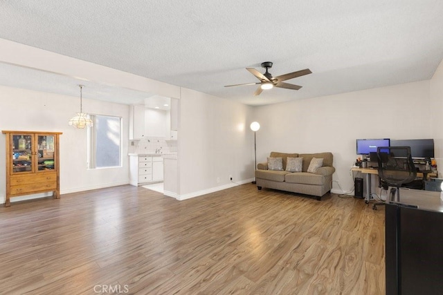 living room featuring ceiling fan with notable chandelier, a textured ceiling, and light wood-type flooring