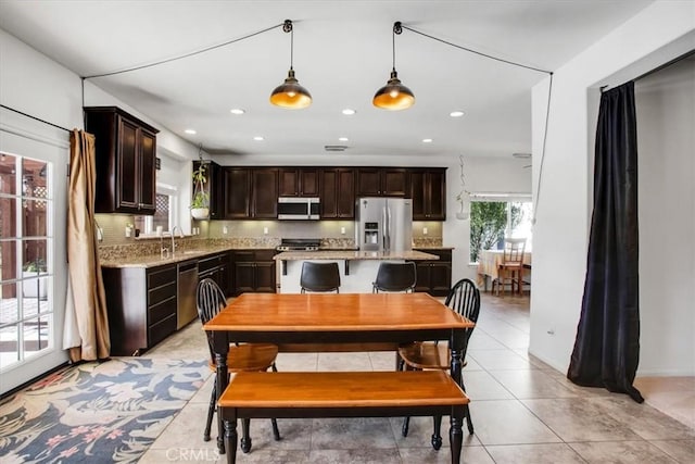 kitchen with sink, stainless steel appliances, light stone counters, pendant lighting, and dark brown cabinets