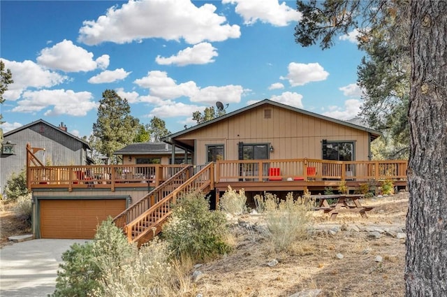 back of property featuring driveway, a garage, and a wooden deck