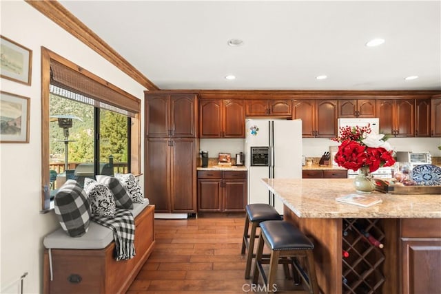 kitchen with crown molding, white refrigerator with ice dispenser, a kitchen breakfast bar, dark wood-type flooring, and recessed lighting