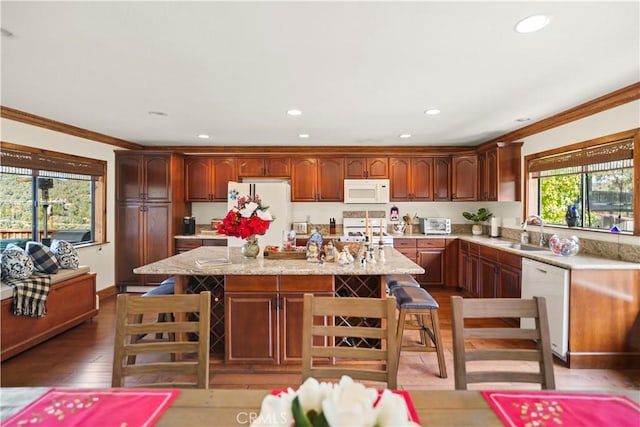 kitchen with a center island, white appliances, hardwood / wood-style flooring, ornamental molding, and a breakfast bar area