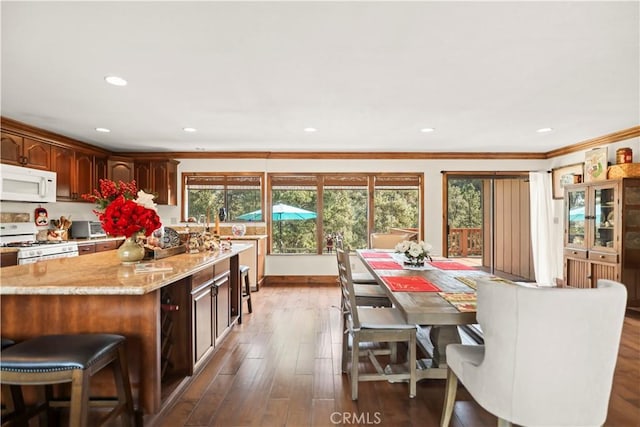 kitchen featuring crown molding, white appliances, light stone countertops, a kitchen island, and dark wood finished floors