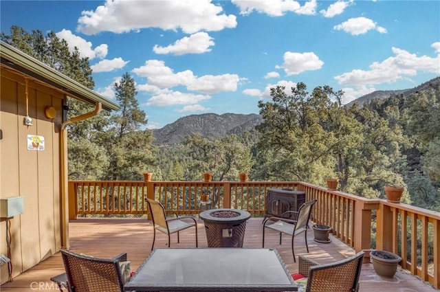 wooden deck with a fire pit, a mountain view, and a view of trees
