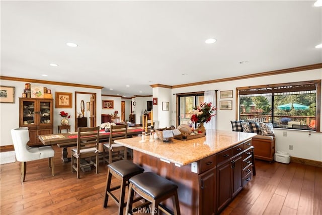 kitchen with dark hardwood / wood-style floors, a center island, ornamental molding, and a breakfast bar