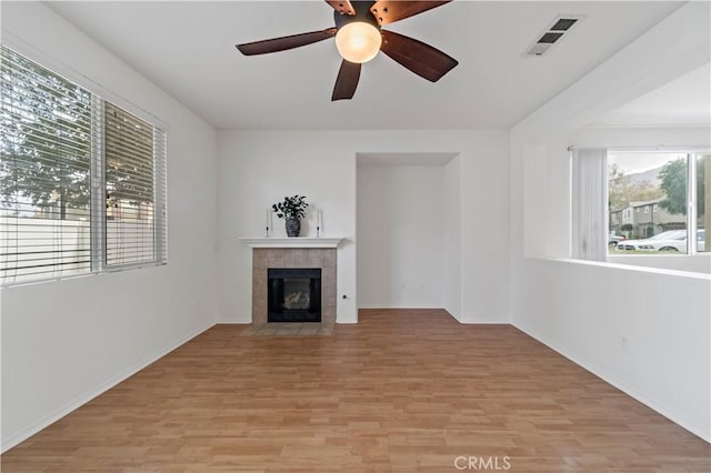 unfurnished living room featuring light wood finished floors, a tile fireplace, visible vents, and a healthy amount of sunlight