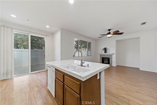 kitchen featuring visible vents, brown cabinetry, an island with sink, white dishwasher, and a sink