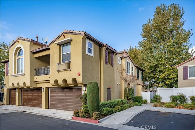 mediterranean / spanish-style home with a tiled roof, an attached garage, fence, and stucco siding