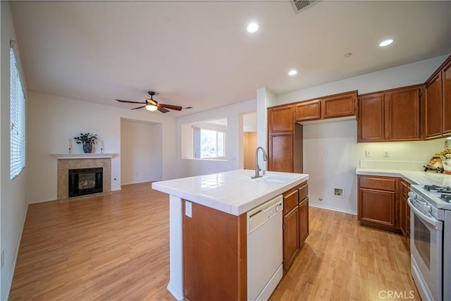 kitchen with white appliances, sink, a center island with sink, light hardwood / wood-style floors, and a tiled fireplace