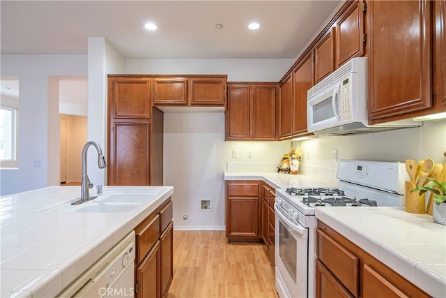 kitchen featuring white appliances, tile counters, light wood-style floors, and a sink