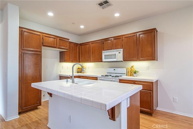 kitchen with white appliances, visible vents, tile counters, brown cabinetry, and a center island with sink