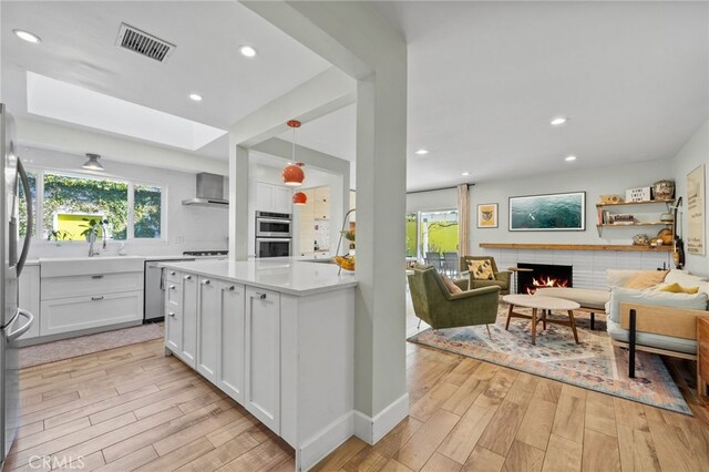 kitchen with pendant lighting, light hardwood / wood-style floors, white cabinetry, and a brick fireplace