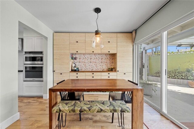 kitchen featuring double oven, light brown cabinets, decorative light fixtures, and light wood-type flooring