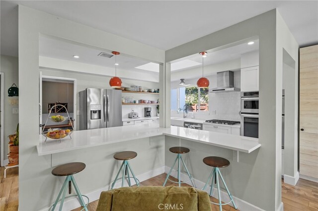 kitchen featuring white cabinets, wall chimney exhaust hood, kitchen peninsula, a breakfast bar area, and stainless steel appliances