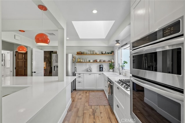 kitchen featuring white cabinetry, sink, pendant lighting, light wood-type flooring, and appliances with stainless steel finishes