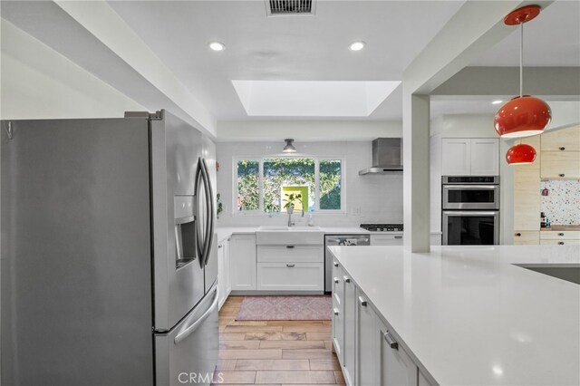 kitchen featuring appliances with stainless steel finishes, a skylight, decorative light fixtures, light hardwood / wood-style flooring, and white cabinets