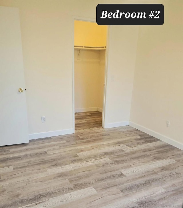 unfurnished bedroom with light wood-type flooring, a spacious closet, and a closet