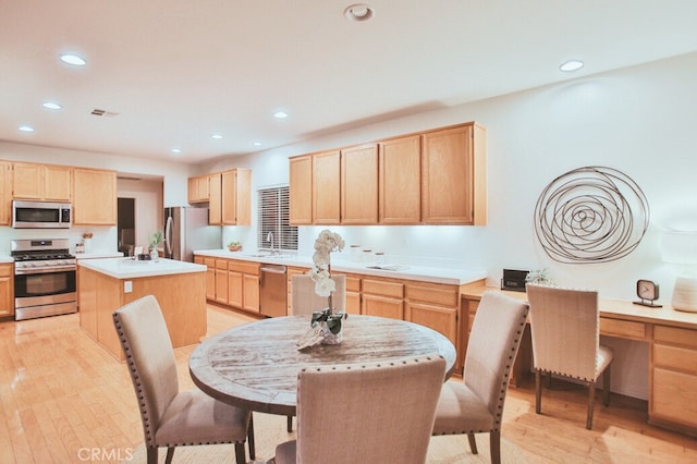 kitchen with appliances with stainless steel finishes, light brown cabinets, a center island, light hardwood / wood-style flooring, and sink