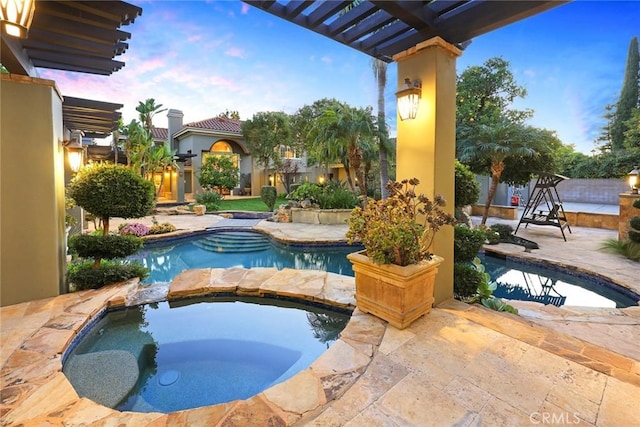 pool at dusk featuring an in ground hot tub and a patio