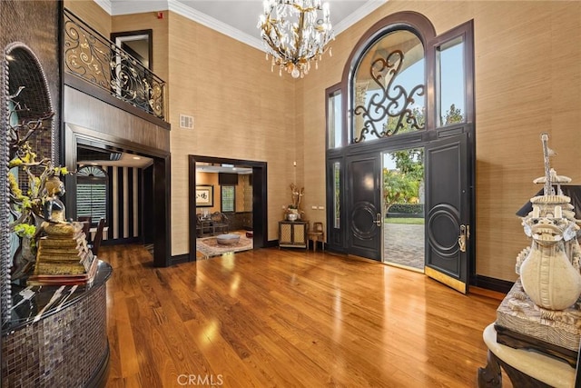 foyer with wood-type flooring, a towering ceiling, plenty of natural light, and a notable chandelier