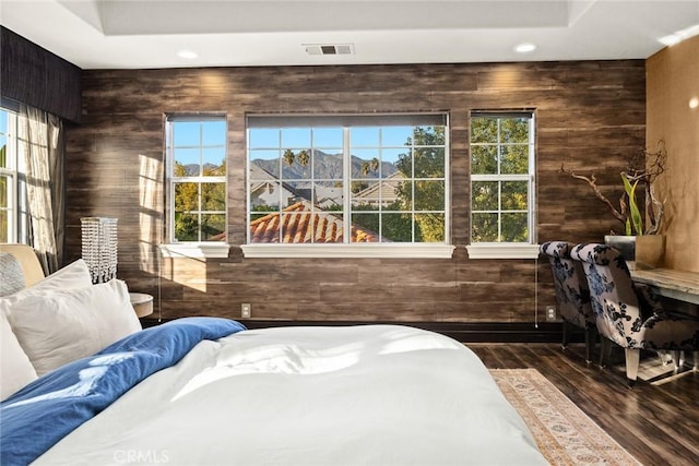 bedroom with dark hardwood / wood-style floors, wooden walls, and multiple windows