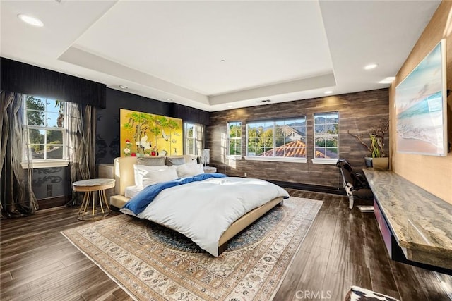 bedroom featuring wooden walls, a raised ceiling, multiple windows, and dark wood-type flooring